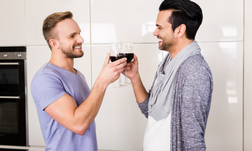 Gay couple toast wine glasses in kitchen